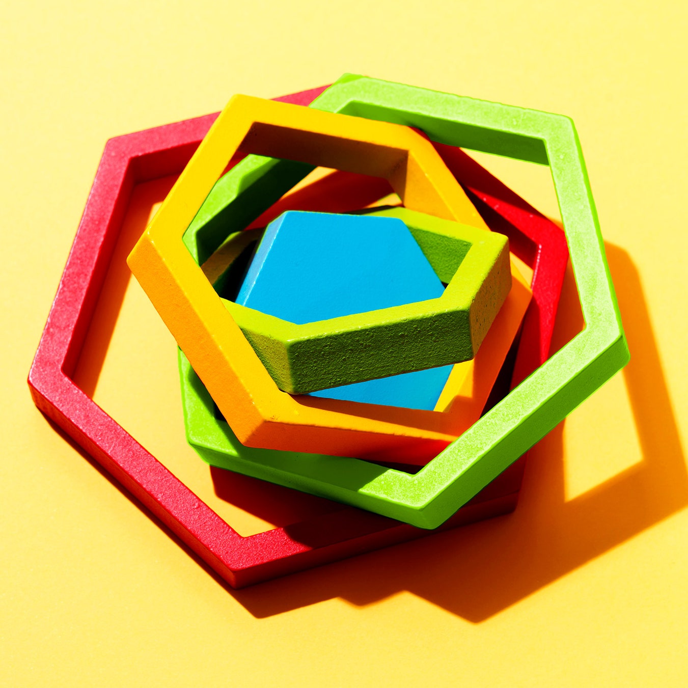 Red green yellow and blue hexagonal wooden blocks in a messy pile on a yellow background